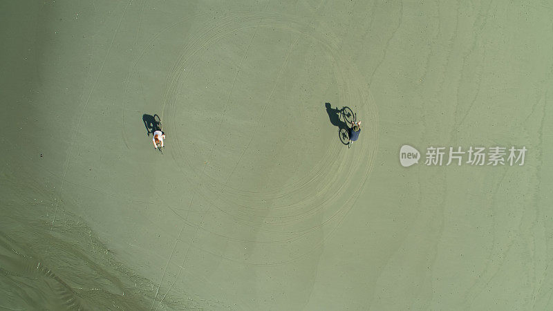 Top Down无人机拍摄的男人和女人骑自行车在海滩上的圈子